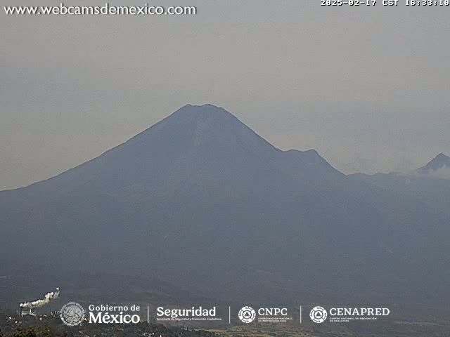 A hazy view shows a large, dark-colored mountain range under a light gray sky.