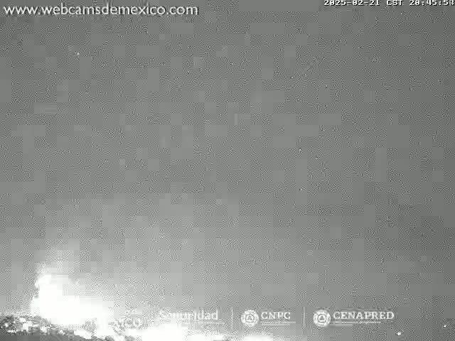 A nighttime, low-light image shows a bright, hazy glow on the horizon under a dark sky.