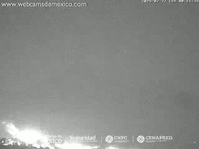A low-light, nighttime outdoor image shows a volcanic eruption with bright white emissions at the bottom of the frame against a gray sky.