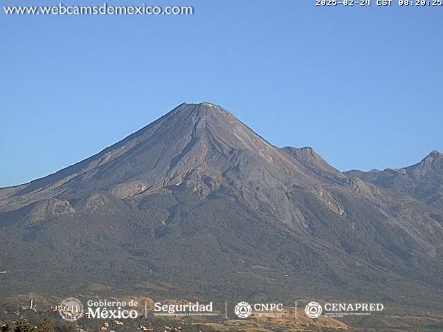 A large, grey volcanic mountain range is visible under a clear blue sky.