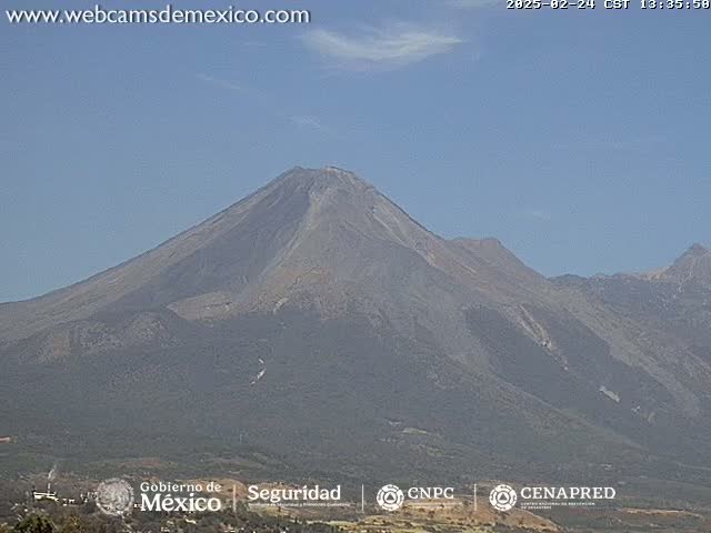 A large, hazy volcano is seen under a mostly clear sky.