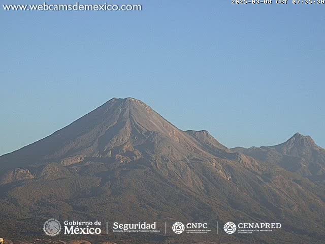 Under a clear sky, a large, dark-grey volcanic mountain range is visible, with one peak significantly taller than the others.