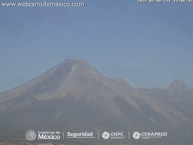 A large, grey volcano is visible under a clear, light-blue sky.