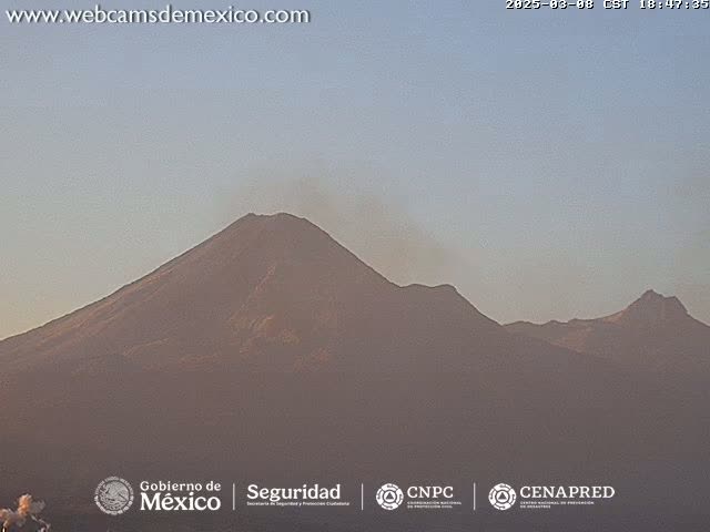 A distant view of a volcanic mountain range under a clear, pale sky at dusk or dawn.