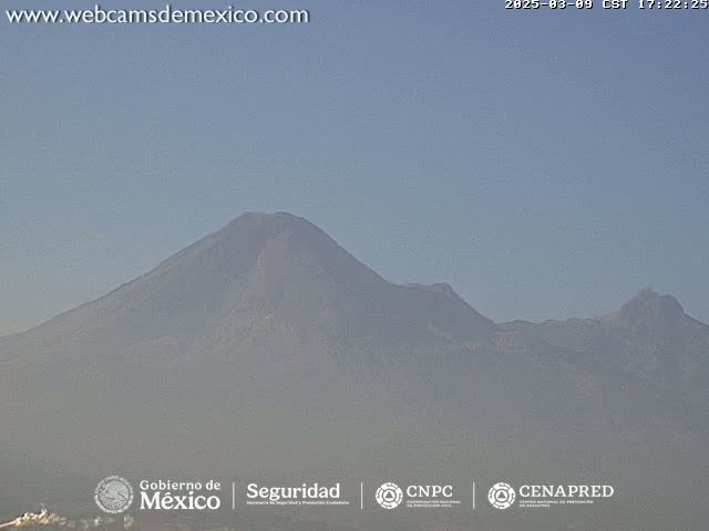 A hazy view shows a large, dark mountain range under a clear, light-blue sky.
