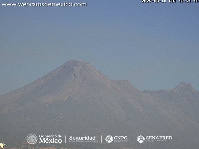 A hazy view shows a large, dark-colored mountain range under a clear, light-blue sky.
