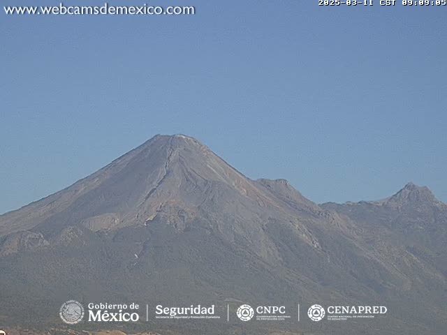 A large, dark-grey volcanic mountain range is visible under a clear, light-blue sky.