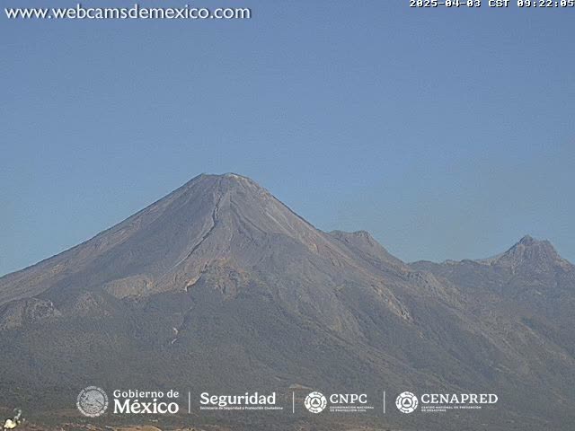A large, dark-grey volcano dominates the landscape under a clear, light-blue sky.