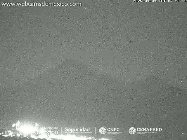 A low-light, nighttime image shows a dark, possibly cloudy sky over a dimly lit landscape.