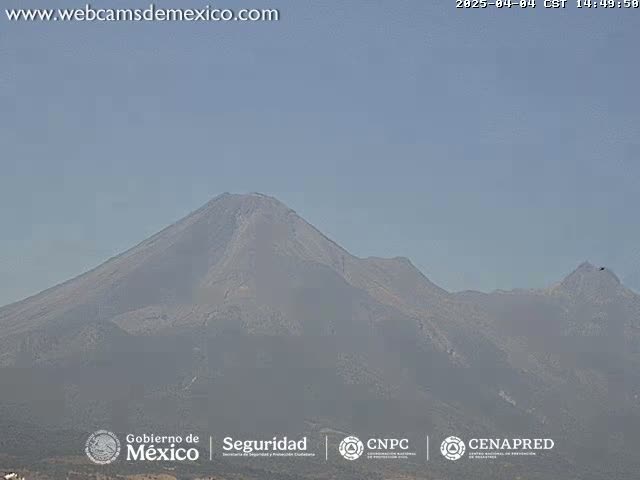 A hazy view of a large, gray mountain range under a clear, light-blue sky.