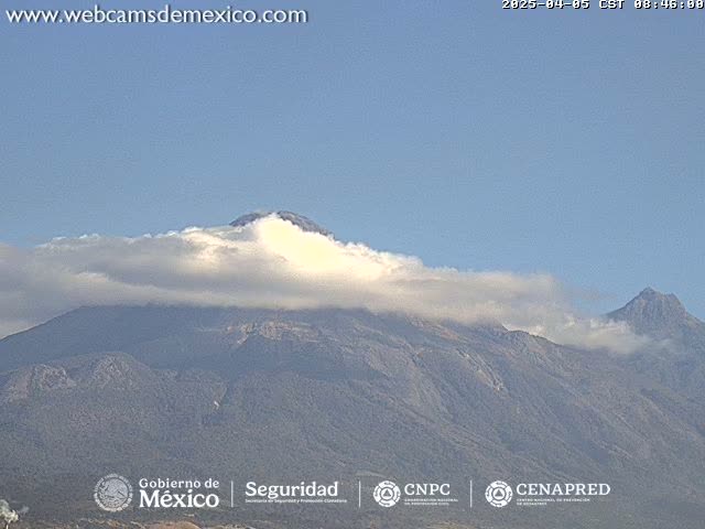 A mountain range partially covered in clouds under a clear blue sky.