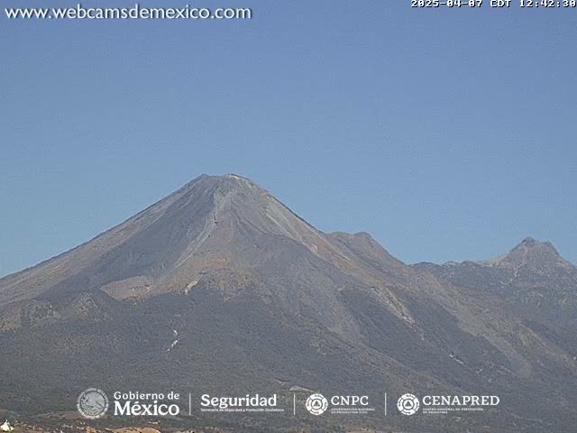 A large, dark-grey volcanic mountain range is visible under a clear, light-blue sky.