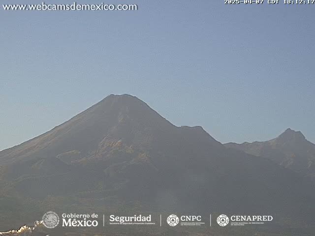 A hazy view of a large, dark mountain range under a clear, light-blue sky.