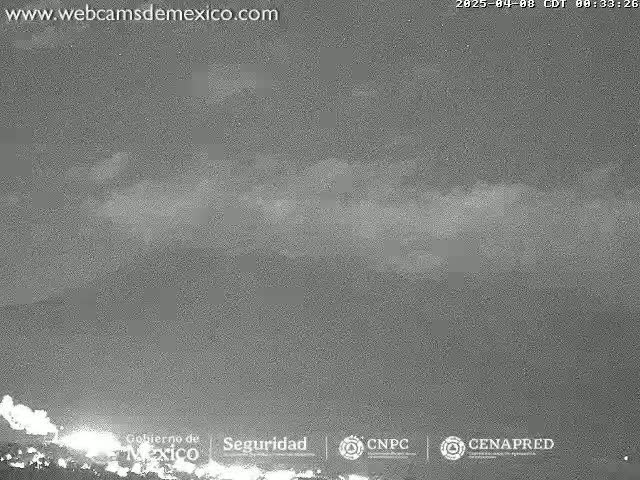 A low-light nighttime image shows a distant, low-lying cloud formation or possibly volcanic emissions under a mostly clear sky.