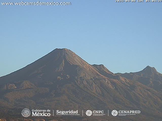 A long shot of a volcanic mountain range under a clear, light-blue sky.