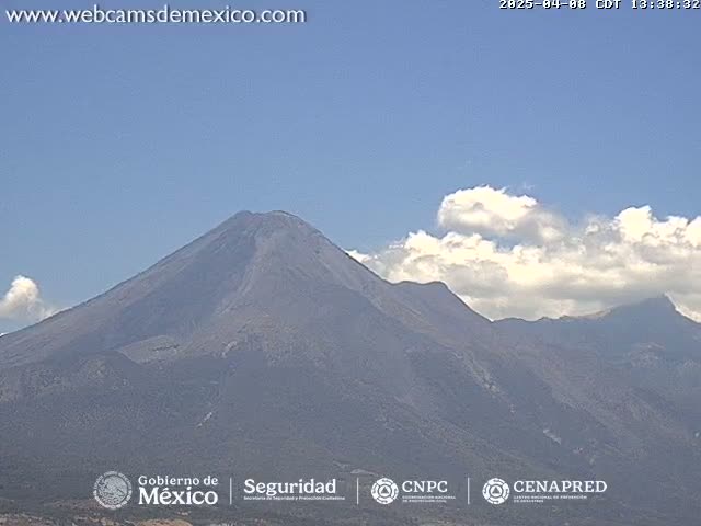 A large, dark gray volcano is visible under a mostly clear blue sky with some fluffy white clouds.