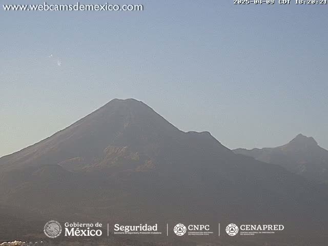 A hazy view of several large, dark mountains under a clear, light-blue sky.