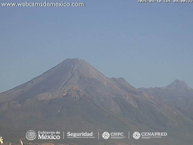 A long shot shows a range of volcanic mountains under a clear, light-blue sky.