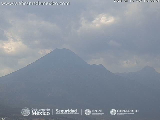 A hazy, overcast sky hangs over a range of dark, distant mountains, one of which is a prominent volcano.