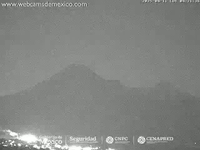 A low-light, nighttime view shows a dark, hazy landscape with a mountain range in the distance under a mostly clear sky.