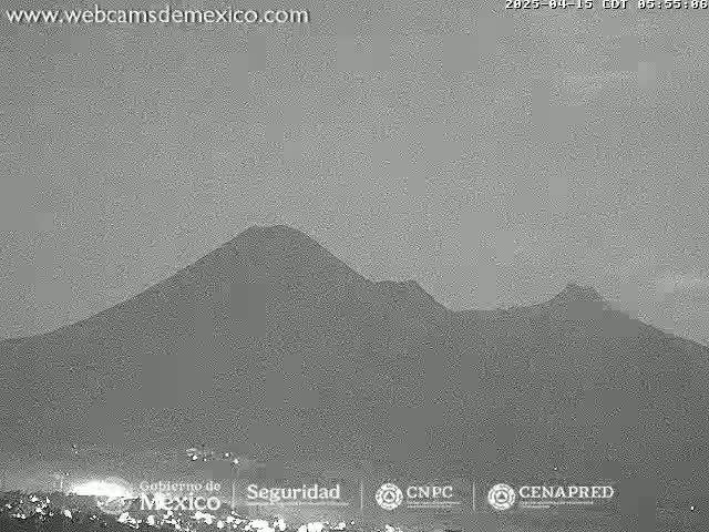 A grayscale image shows a volcanic mountain range under a light gray, overcast sky.