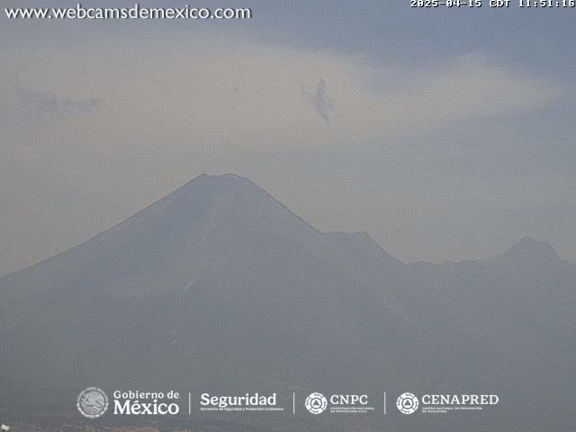 A hazy view shows a large, dark mountain range under a mostly clear sky.