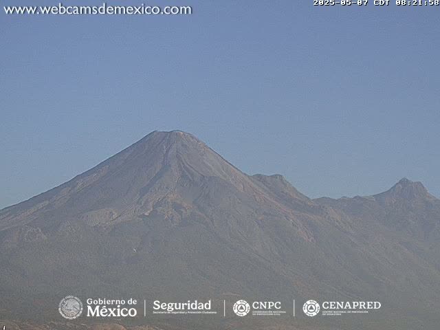 A large, dark-grey volcanic mountain range is visible under a clear, light-blue sky.