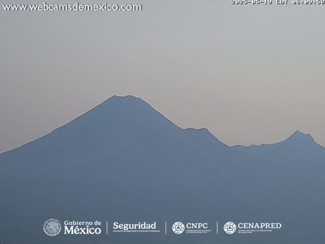 A hazy view shows a large, dark-blue mountain range under a light-grey sky.