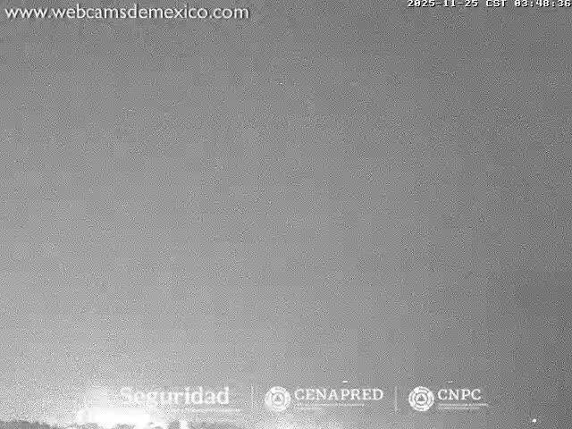 A grainy, monochromatic image captured at night shows a bright, glowing light source emerging from the bottom against a heavily overcast or hazy sky.