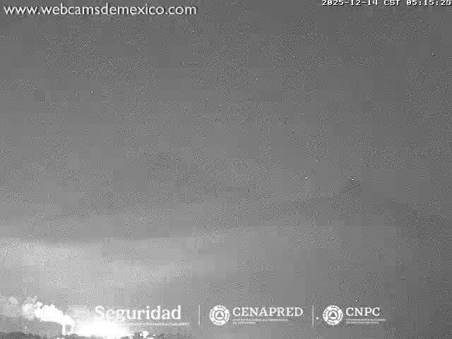 A grainy, monochromatic image captured at night shows a bright, glowing light source emerging from the bottom against a heavily overcast or hazy sky.