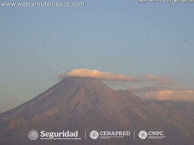 A grainy, monochromatic image captured at night shows a bright, glowing light source emerging from the bottom against a heavily overcast or hazy sky.