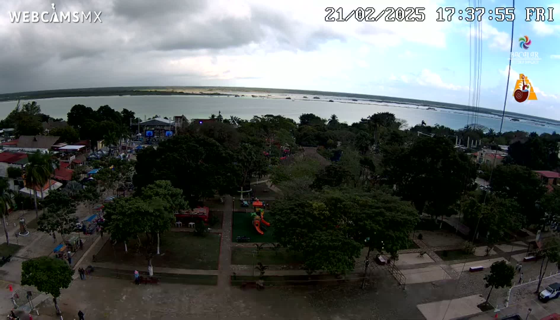 An aerial view shows a town square with a playground and a body of water under an overcast sky.