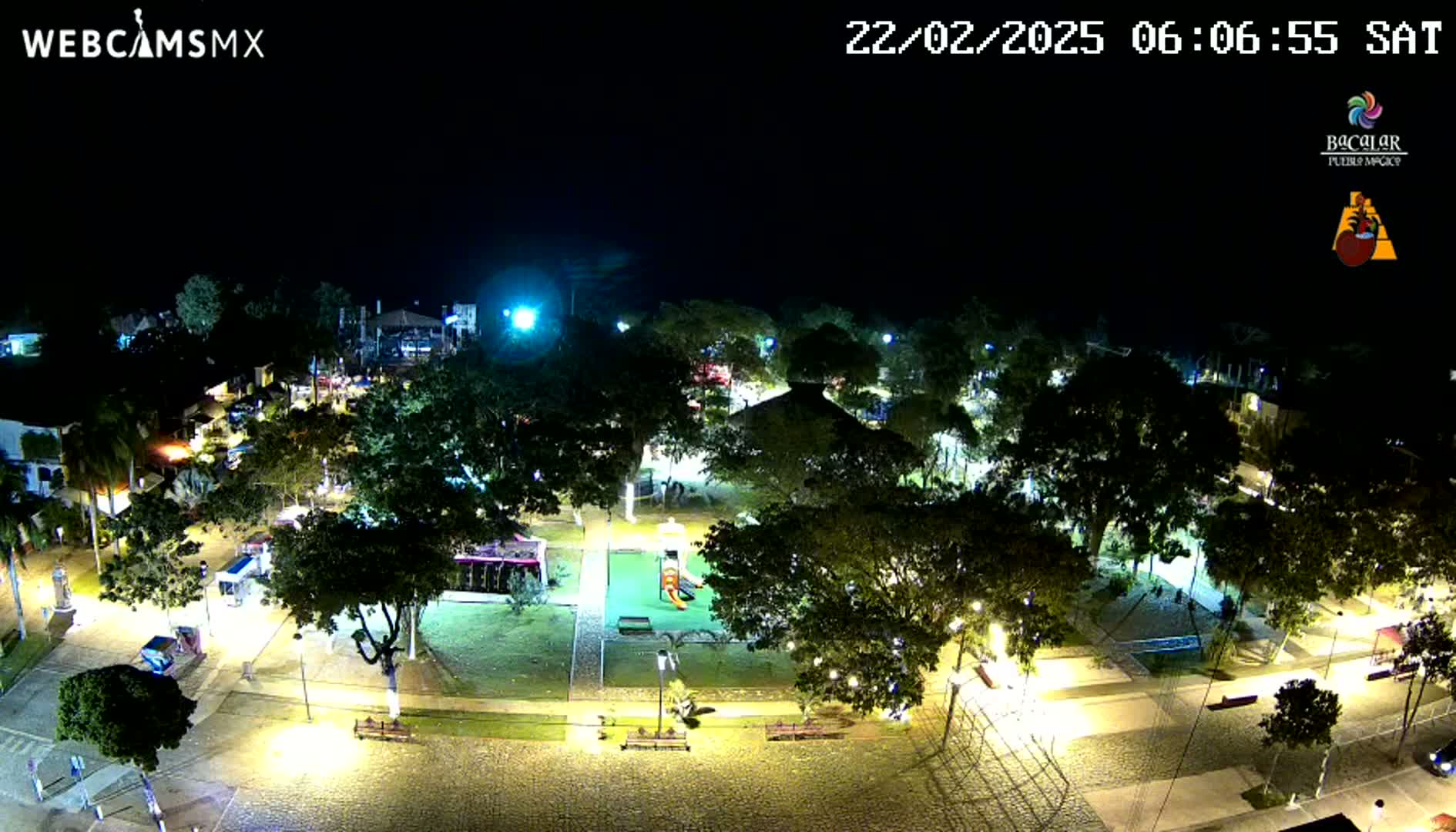 An aerial nighttime view of a park-like area with illuminated pathways, trees, and playground equipment.
