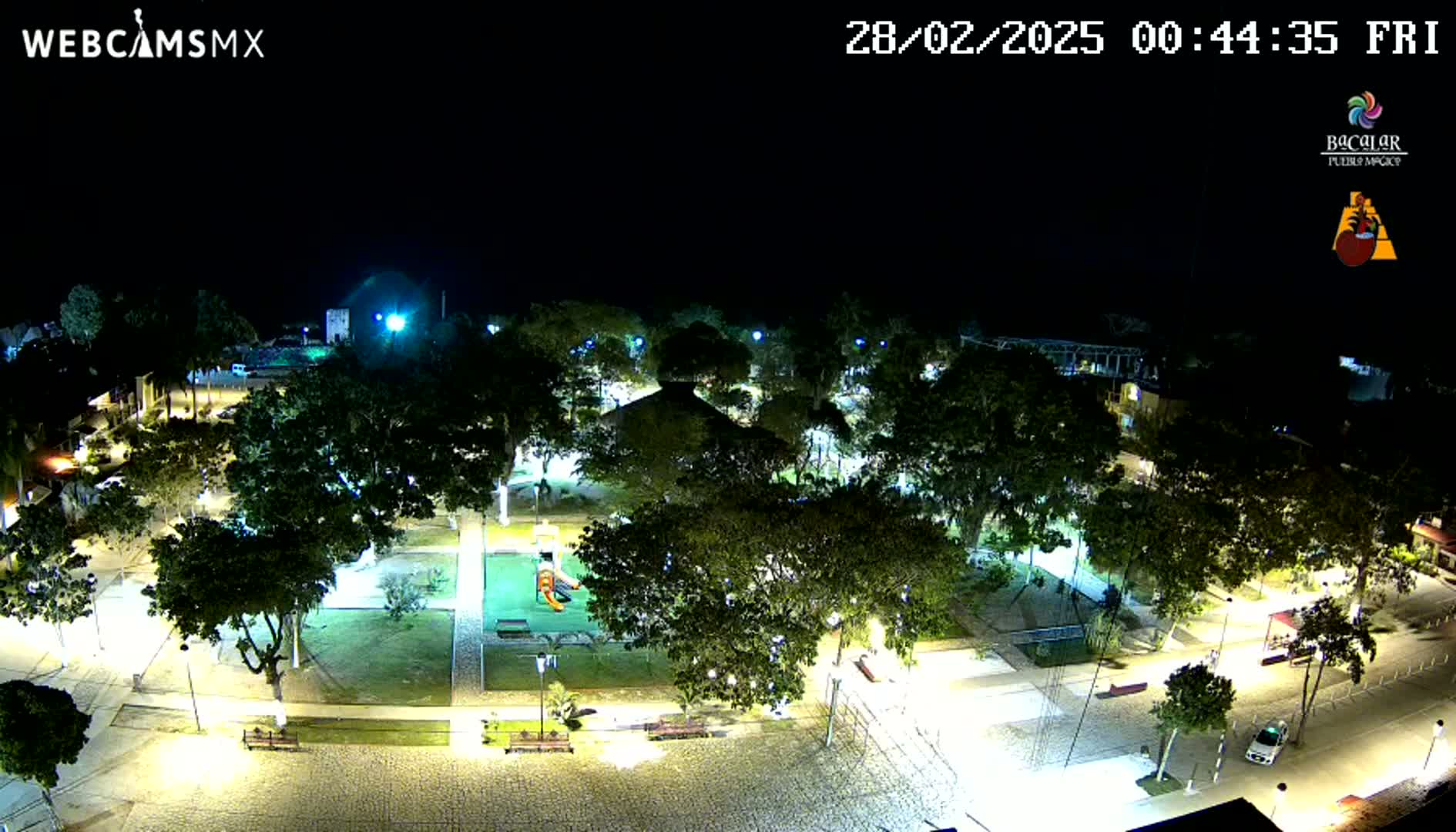 A nighttime aerial view of a park with a playground, surrounded by illuminated trees and streets.