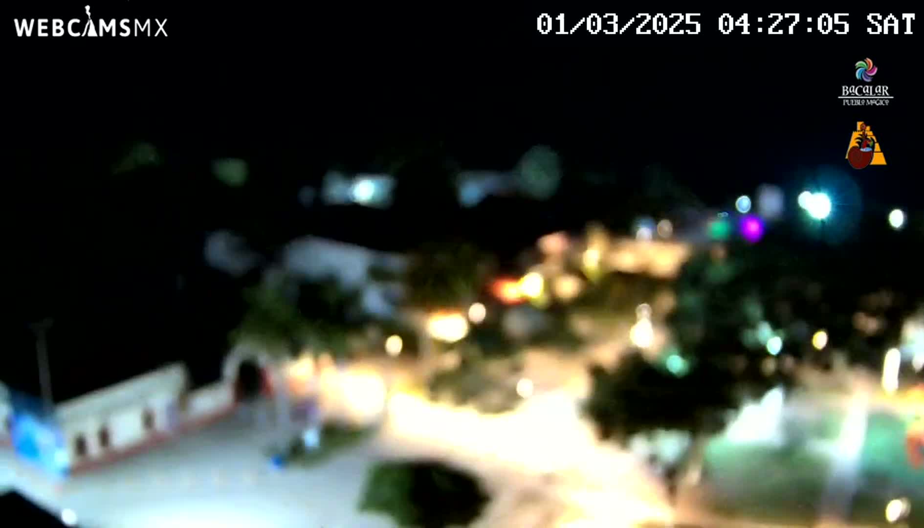 A blurry, nighttime aerial view of a town square with many lights and some vegetation.