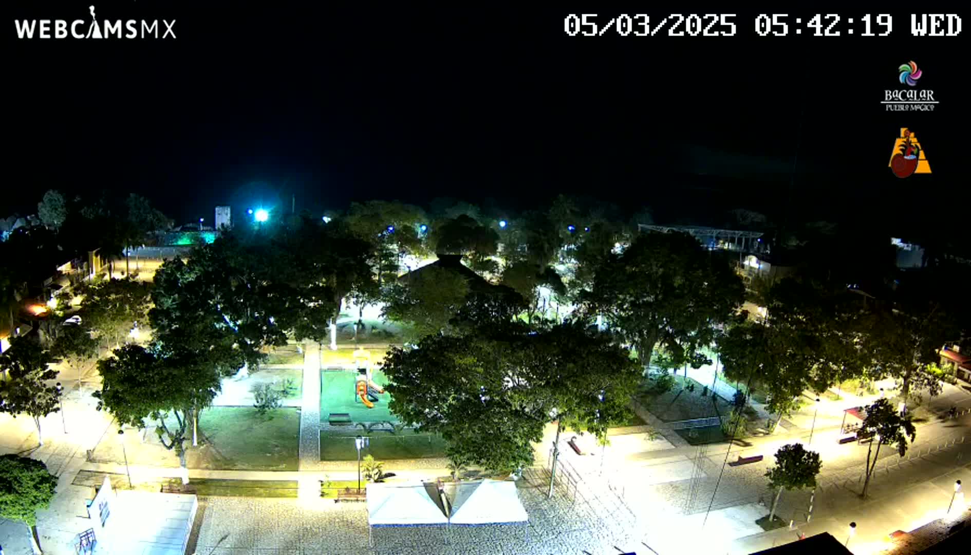 A nighttime aerial view of a park with illuminated pathways, trees, and playground equipment.