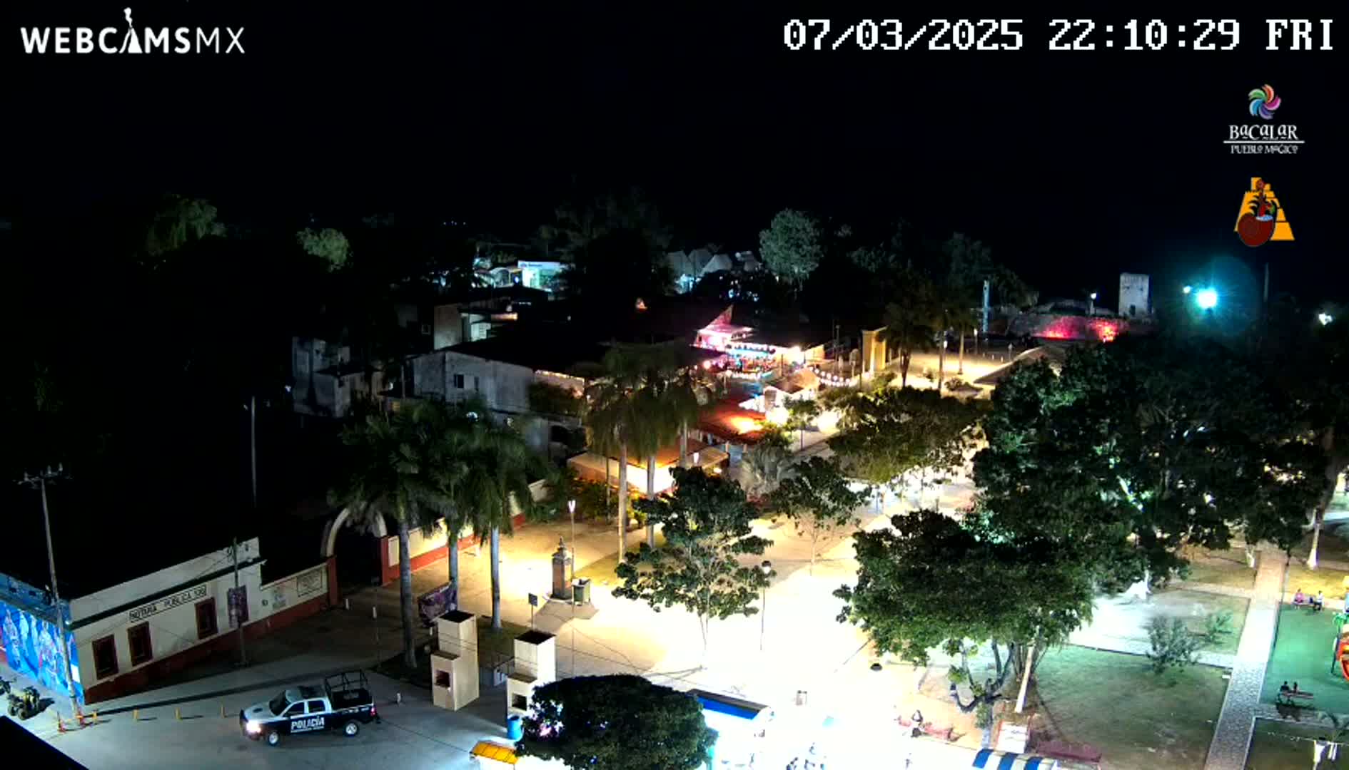 A nighttime aerial view of a town square with illuminated buildings and trees under a clear, dark sky.