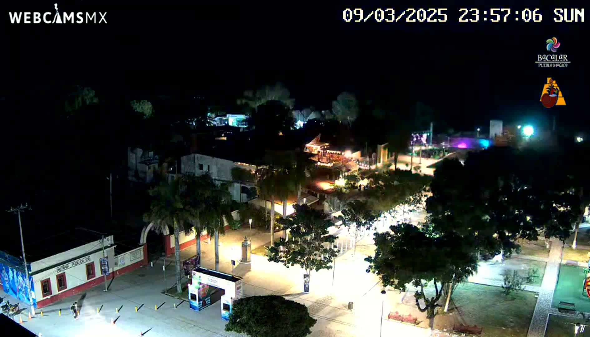An illuminated town square at night, surrounded by buildings and trees under a clear, dark sky.
