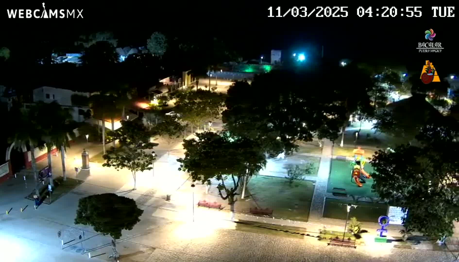 An elevated nighttime view of a town square with a playground, illuminated by streetlights under a clear sky.