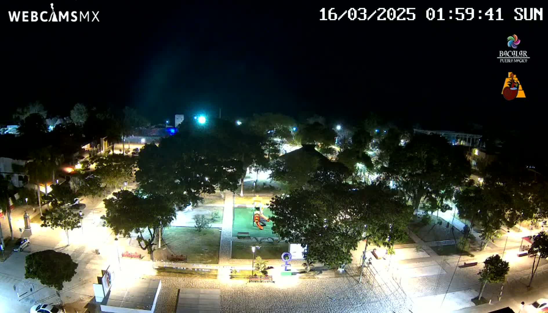 An illuminated park at night, surrounded by buildings and streets, under a clear, dark sky.