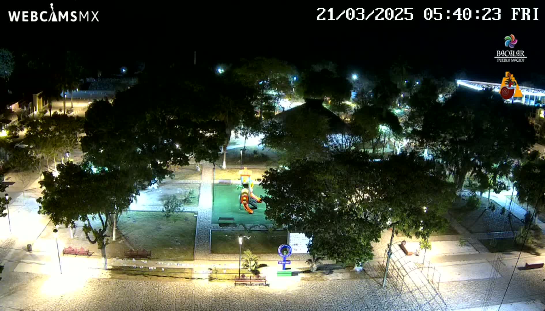 A nighttime aerial view of a park with a playground, illuminated by streetlights, under clear skies.