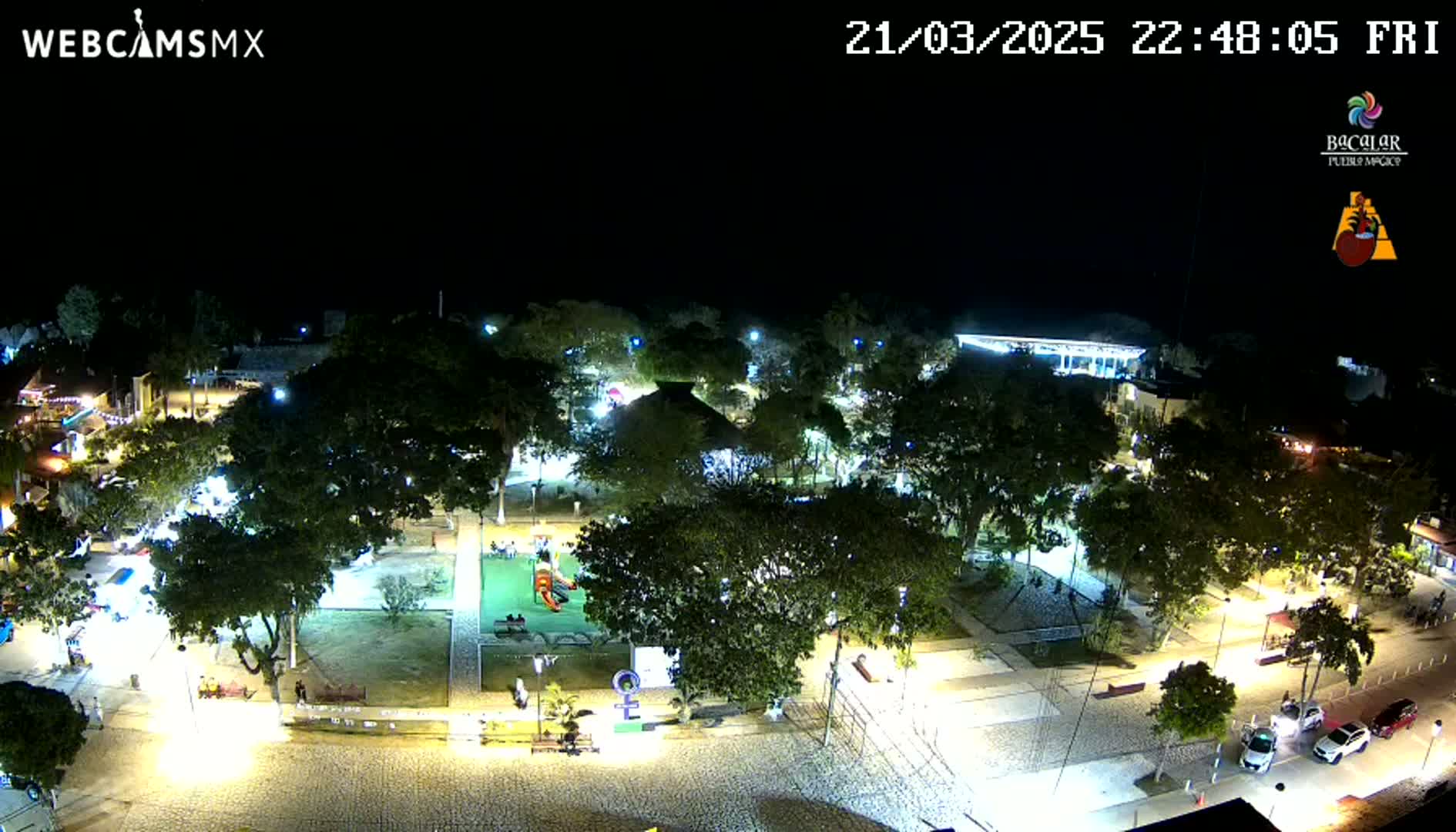 A nighttime aerial view of a park with a playground, surrounded by buildings and trees, under a clear, dark sky.
