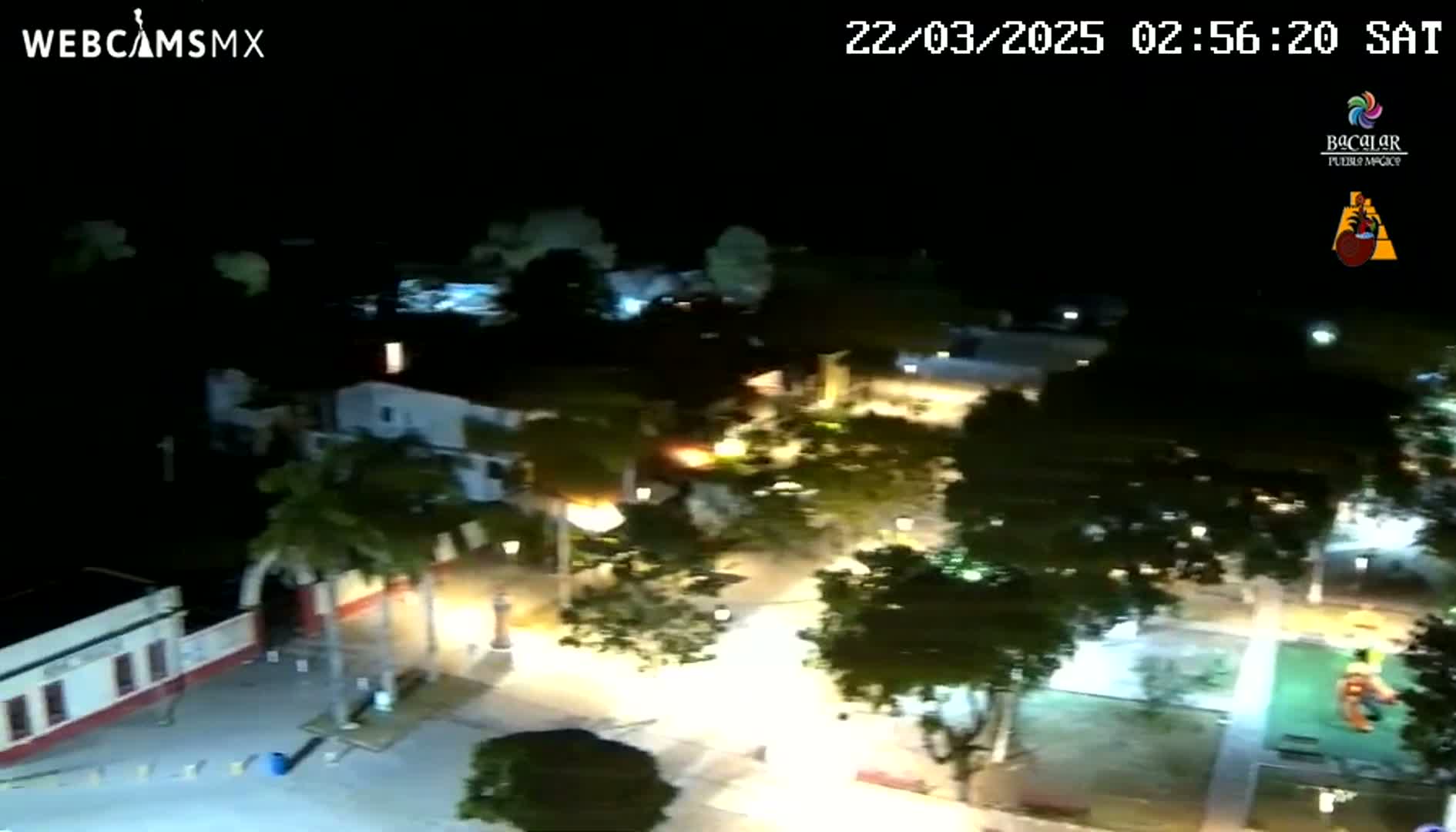 An aerial nighttime view of a town square with illuminated buildings and trees under a clear, dark sky.