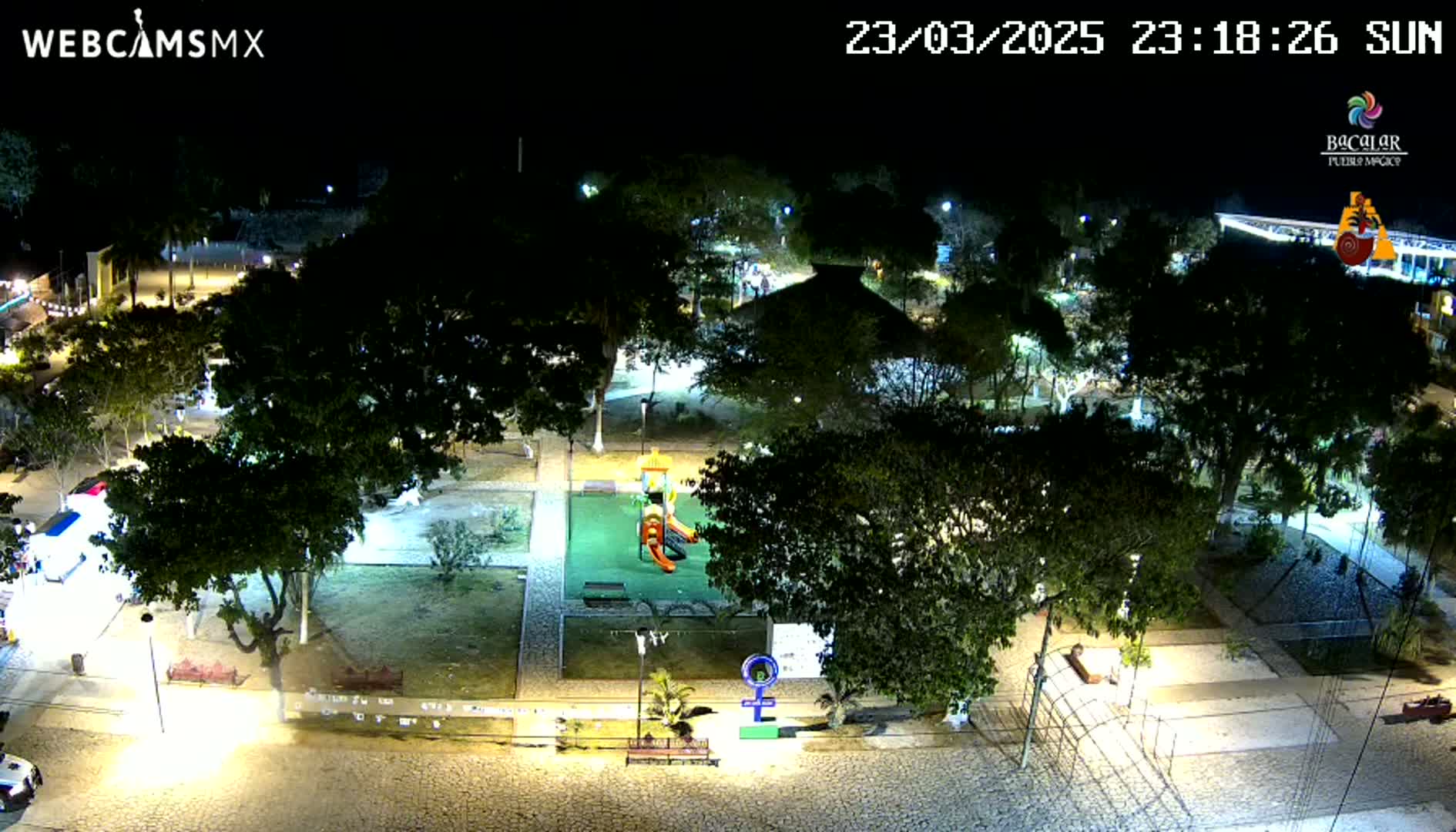 A nighttime aerial view of a park with a playground, surrounded by trees and illuminated by streetlights.
