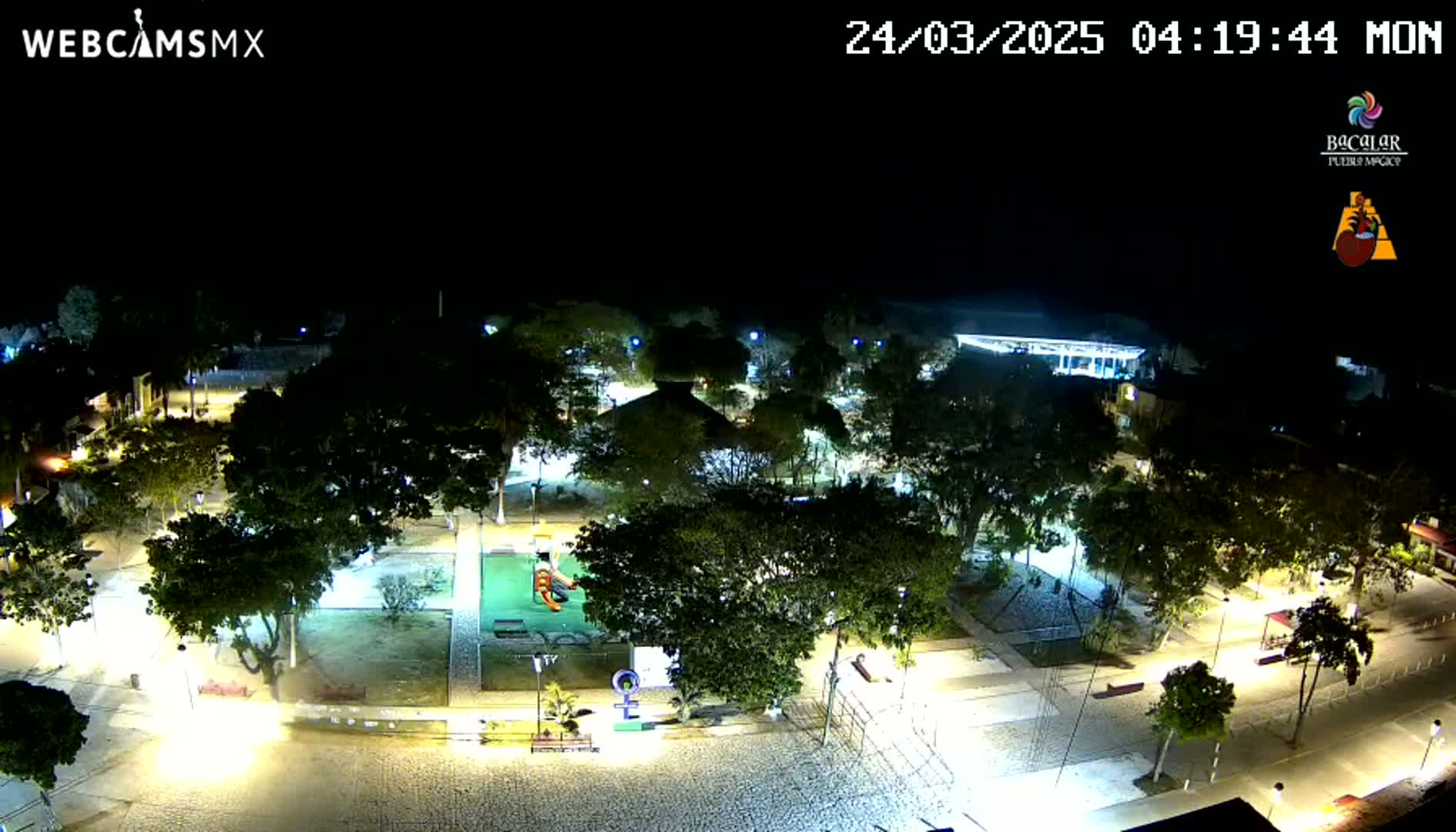An illuminated nighttime park with many trees and walkways, under a clear sky.