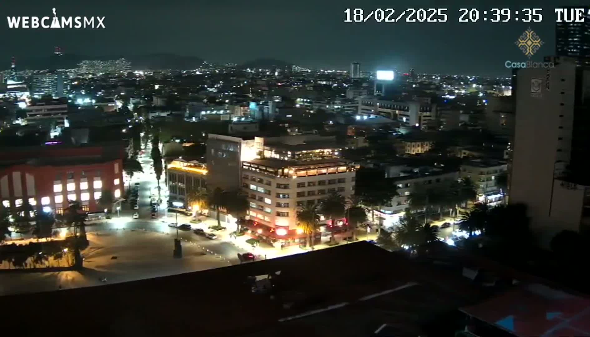 A nighttime aerial view of a city with brightly lit buildings and streets, under a clear sky.