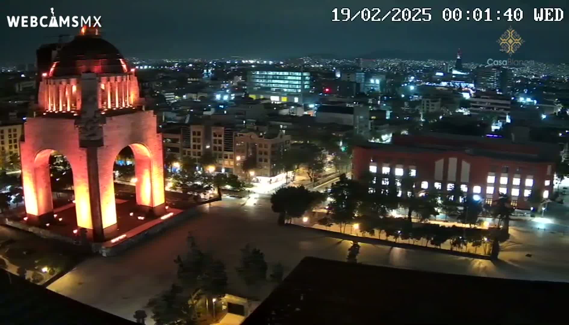 A brightly lit monument stands in a city square at night, surrounded by other illuminated buildings under a clear, dark sky.