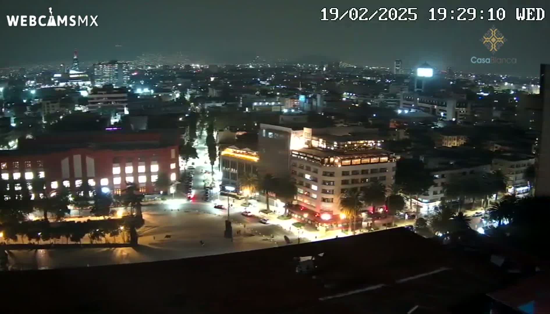 A nighttime, aerial view of a city showing illuminated buildings and streets, with some scattered traffic.