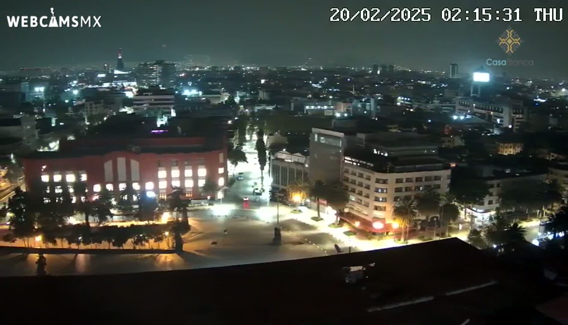 A nighttime, aerial view of a city square and surrounding buildings, illuminated by streetlights under a clear sky.