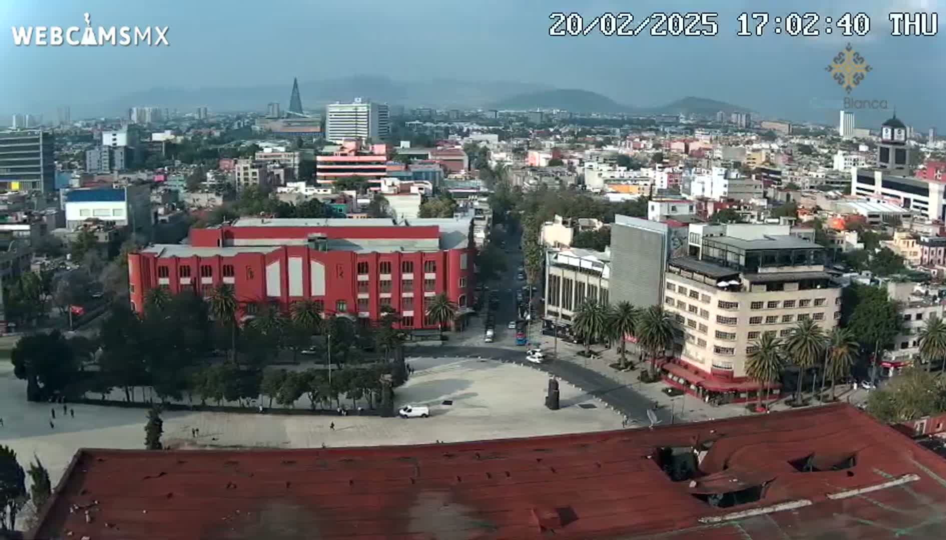 A high-angle view of a city square and surrounding buildings on a hazy day, with palm trees lining the streets.
